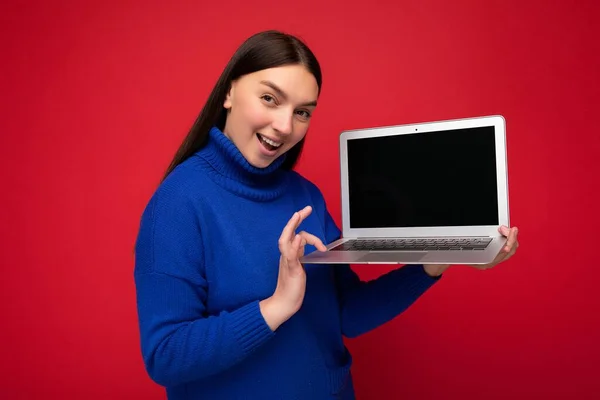 Foto de una hermosa mujer joven sosteniendo computadora portátil mirando a la cámara aislada sobre un fondo colorido —  Fotos de Stock