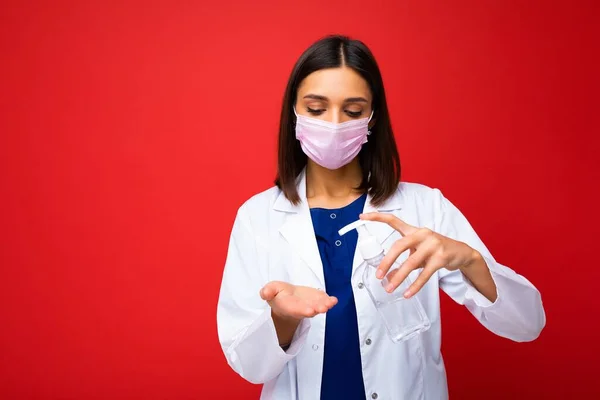 Consigli medici e protezione della salute durante l'epidemia di coronavirus. Giovane donna medico in maschera protettiva, cappotto bianco mostra antisettico nelle sue mani, isolato su sfondo — Foto Stock