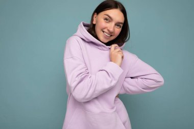 Güzel, pozitif gülümseyen, şık kıyafetler giyen, renkli bir arka planda dikilip fotokopi çeken ve kameraya bakan yetişkin bir kadının fotoğrafı.