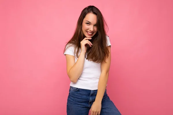 Foto porträtt av ung vacker leende hipster brunett kvinna i vit t-shirt med mockup. Sexig bekymmerslös kvinnlig person poserar isolerad nära rosa vägg med tomt utrymme i studio. Positiv modell — Stockfoto