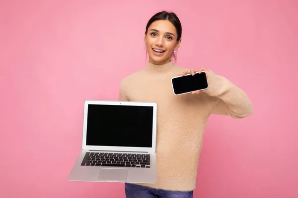 Fénykép bájos szép mosolygós fiatal nő sötét hajjal nézi kamera gazdaság számítógép laptop és mobil telefon üres monitor képernyő modellezés és másolás helyet viselő fény — Stock Fotó