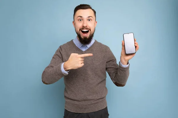 Photo of handsome smiling adult male person good looking wearing casual outfit standing isolated on background with copy space holding smartphone showing phone in hand with empty screen display for — Stock Photo, Image