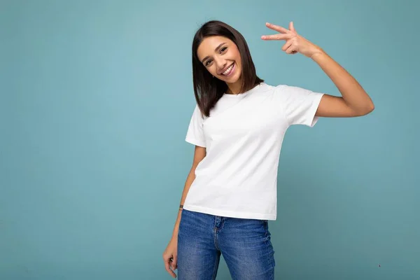 肯定的な笑顔喜び若い美しいブルネットの女性で誠実な感情を身に着けていますカジュアルホワイトTシャツのためにモックアップのために隔離された青の背景とともにコピースペース — ストック写真