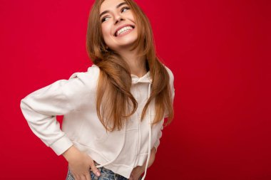 Çekici, mutlu, günlük kıyafetler giyen, renkli arka planda tek başına duran, yan tarafa bakan genç bir kadın.