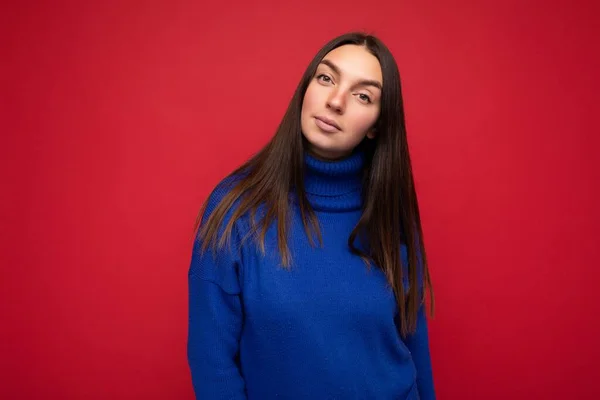 Young self-confident beautiful brunette woman with sincere emotions isolated on background wall with copy space wearing casual trendy blue sweater looking at camera
