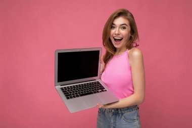 Güzel sarışın bir kadın bilgisayarında dizüstü bilgisayar tutuyor pembe ekinlerle pembe arka planda izole edilmiş kameraya bakıyor.