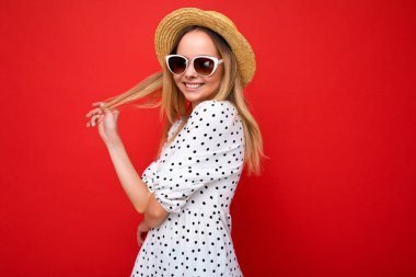 Çekici, mutlu, gülümseyen, günlük şık kıyafetler giyen ve renkli arka plan duvarında izole edilmiş modern güneş gözlüğü takan genç, sarışın kadın kameraya bakıyor.