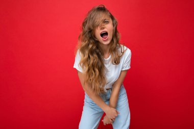 Genç, mutlu, neşeli, beyaz tişört giyen, kırmızı arka planda izole edilmiş, boş alan ve bağıran sarışın bir kadın.