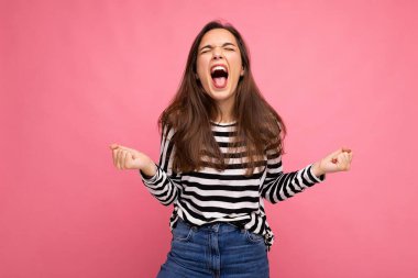 Genç, pozitif, mutlu, çekici ve samimi duyguları olan çekici bir kadın. Pembe arka planda izole edilmiş ve zaferi kutlayan, evet diye bağıran bir kazak.