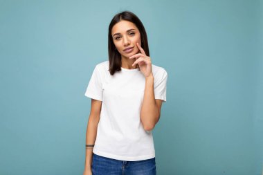 Çekici, düşünceli, beyaz tişörtlü, rahat bir esmer kadın. Mavi arka planda izole edilmiş.