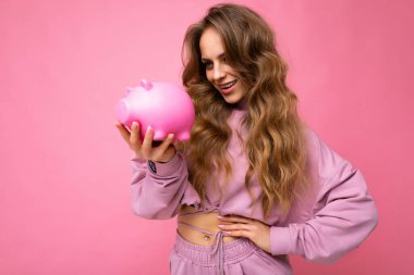 Mutlu, pozitif gülümseyen, uzun, dalgalı, sarı saçlı, samimi, pembe kapüşonlu pembe kapüşonlu fotograflı çekici bir kadının portresi.