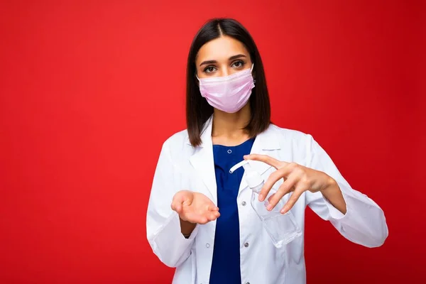 Doctors advice and health protection during coronavirus epidemic. Young woman doctor in protective mask, white coat shows antiseptic in her hands, isolated on background