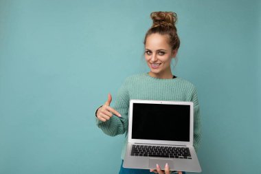 Güzel, mutlu, esmer, kıvırcık saçlı genç bir kadının fotoğrafı. Kameraya bakıp netbook 'u işaret ediyor. Bilgisayarı elinde tutuyor.
