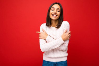 Güzel, mutlu gülümseyen, sevimli, sevimli, hoş esmer, şık, hafif örgü formalı kadın. Kırmızı arka plan duvarına izole edilmiş, boş alan ve keyfini çıkarıyor.