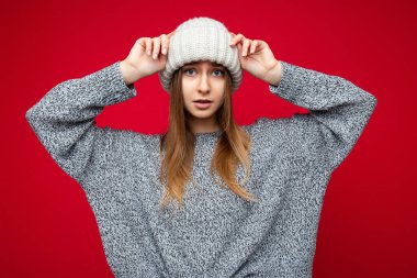 Çekici, şaşkın, genç, esmer, sarışın bir kadın renkli arka plan duvarının üzerinde dikiliyor günlük şık kıyafetler giyiyor ve kameraya bakarak yüz ifadelerini gösteriyor.