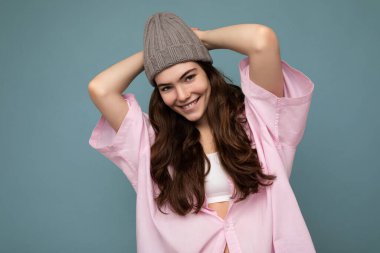 Çekici, gülümseyen, mutlu, esmer kadın renkli arka plan duvarının üzerinde soyutlanmış, günlük şık kıyafetler giymiş kameraya bakarken yüz ifadelerini gösteriyor.