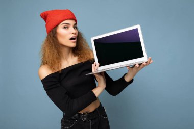 Güzel, şaşkın bir şekilde, açık ağızlı, esmer, kıvırcık saçlı, siyah bluzlu, kırmızı ve turuncu paçavralı bir kadını açık mavi arka planda tutarken görmek beni şaşırttı.