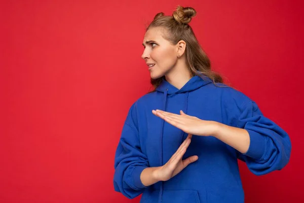 Photo of emotional young pretty blonde female person with two horns with sincere emotions wearing hipster bright blue pullover isolated over red background with copy space and showing timeout gesture — Stock Photo, Image