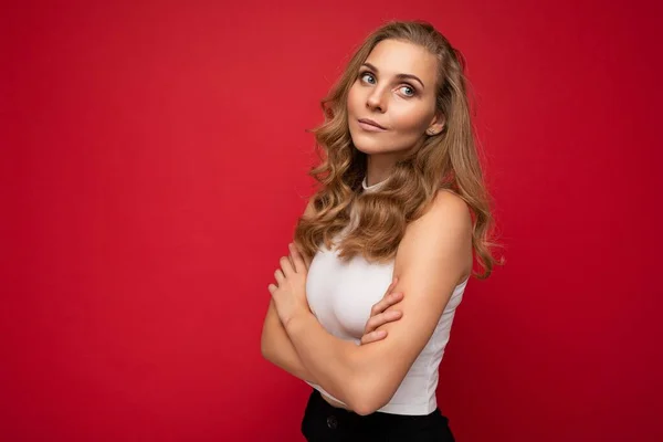 Retrato de jovem bonita muito auto-confiante pensativo loira empresária com emoções sinceras vestindo casual top branco isolado sobre fundo vermelho com espaço vazio com os braços cruzados — Fotografia de Stock