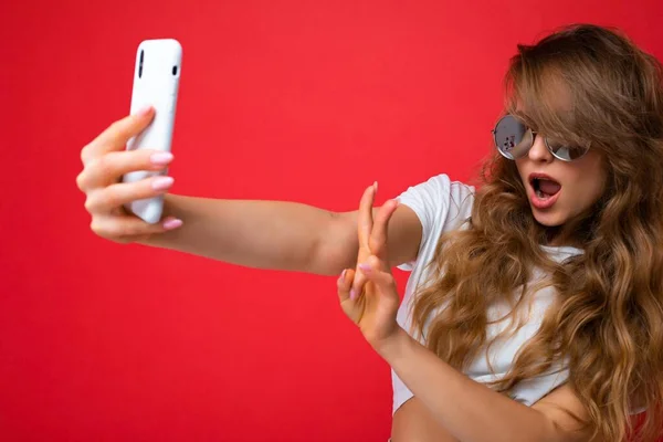 Foto close-up de bela jovem segurando telefone celular tirando foto selfie usando câmera de smartphone usando óculos de sol roupa elegante todos os dias isolado sobre fundo de parede colorido olhando para — Fotografia de Stock