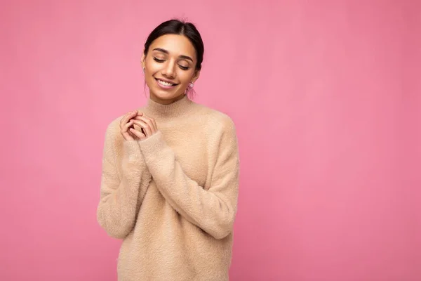 Foto de la joven hermosa mujer morena sonriente feliz usando jersey beige. Sexy persona femenina despreocupada posando aislado cerca de la pared rosa en el estudio con espacio libre. Modelo positivo con maquillaje natural —  Fotos de Stock