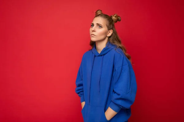 Retrato de triste cansado joven atractiva mujer rubia guapa con dos cuernos con emociones sinceras usando sudadera con capucha azul brillante casual aislado sobre fondo rojo con espacio libre — Foto de Stock