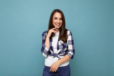 Genç, mutlu, neşeli, tatlı, esmer, samimi duyguları olan, çek gömlek giyen, mavi arka planda izole edilmiş, fotokopi alanı ile izole edilmiş bir kadın.