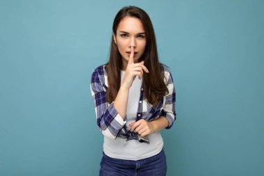 Samimi duyguları olan genç, esmer, modaya uygun bir çek gömleği giyen, mavi arka planda izole edilmiş, boş bir alanda duran ve 