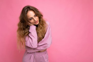 Güzel görünümlü, sevimli, sevimli, sevimli, sevimli, güzel, neşeli, neşeli, dalgalı saçlı, sarışının yakın plan portresi. Pastel arka planda izole edilmiş, şık kıyafetler giyiyor.