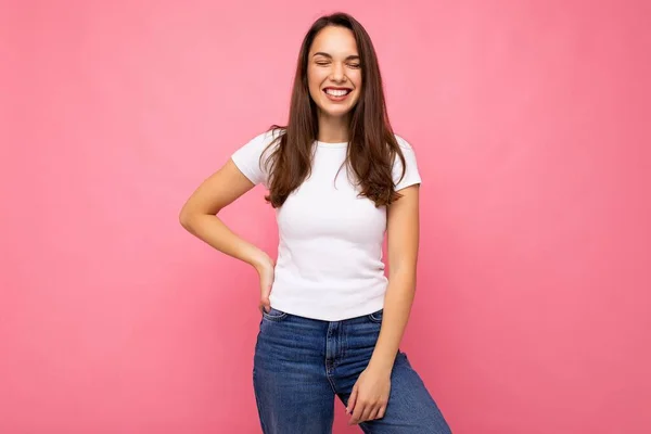 Foto retrato de la joven hermosa mujer morena hipster sonriente en camiseta blanca con maqueta. Sexy persona femenina despreocupada posando aislada cerca de la pared rosa con espacio vacío en el estudio. Modelo positivo —  Fotos de Stock