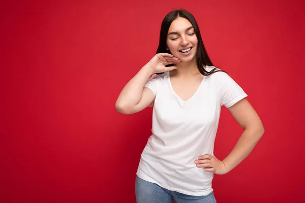 Молодая счастливая привлекательная брюнетка с искренними эмоциями изолирована на задней стенке с копировальным пространством в повседневной белой футболке для макета. Позитивная концепция — стоковое фото