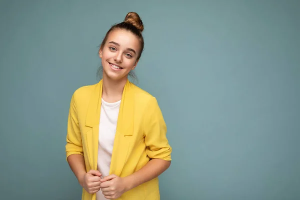 Foto de la hermosa morena sonriente positiva niña usando chaqueta amarilla de moda y camiseta blanca de pie aislado sobre la pared de fondo azul mirando a la cámara —  Fotos de Stock