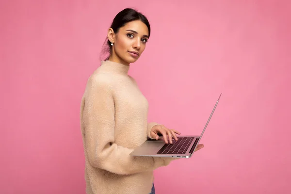 Profil lateral fotografie de fermecătoare femeie destul de tânără care deține laptop izolat peste fundal de perete uitându-se la tastarea camerei pe textul tastaturii și gândindu-se la ceva — Fotografie, imagine de stoc