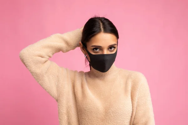 Mladá krásná brunetka žena v opakovaně použitelný virus ochranné masky na tváři proti coronavirus izolované na růžové pozadí zdi — Stock fotografie