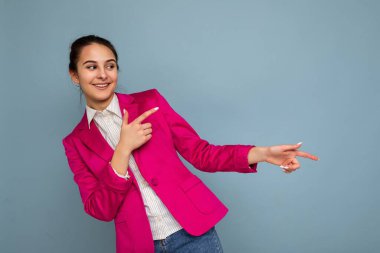 Çekici, güzel, pozitif, mutlu, gülümseyen esmer kadının resmi. Samimi duyguları olan, günlük beyaz gömlek giyen, mavi arka planda izole edilmiş pembe ceketli.