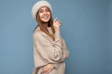 Çekici, gülümseyen, mutlu, esmer, sarışın bir kadın. Renkli arka plan duvarının üzerinde tek başına duruyor. Günlük şık kıyafetler giyiyor ve kameraya bakarak yüz ifadelerini gösteriyor.