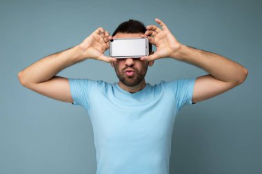 Yakışıklı, yakışıklı, yakışıklı, şık kıyafetler giyen, renkli arka plan duvarında izole bir şekilde duran, akıllı telefon tutan ve telefonu boş ekran ekranlı gösteren yakışıklı bir adam.