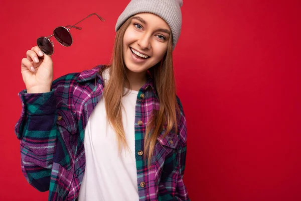 Foto záběr krásné pozitivní mladé brunetky žena na sobě letní ležérní oblečení a držení stylové sluneční brýle izolované přes barevné pozadí zdi při pohledu na kameru — Stock fotografie