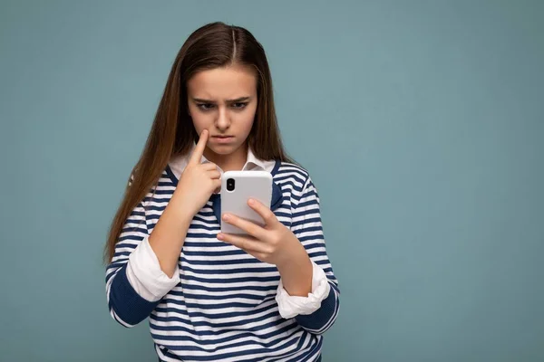 Mooi jong meisje dragen casual kleding staan geïsoleerd over achtergrond surfen op het internet via telefoon kijken naar mobiele scherm — Stockfoto