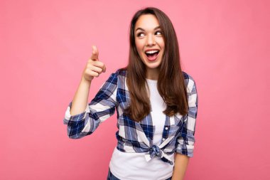 Genç, mutlu, gülümseyen, samimi duyguları olan güzel esmer kadın pembe arka planda izole edilmiş, modaya uygun bir çek gömlek giyiyor.