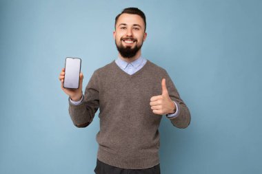 Mutlu gülümseyen yakışıklı yakışıklı yakışıklı güzel giyinen şık kıyafetler giyen renkli arka plan duvarının üzerinde izole edilmiş akıllı telefonu tutan ve boş ekranlı telefonu gösteren