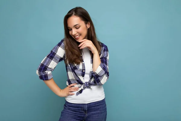 Portrait photo de jeune belle femme brune hipster souriante en chemise et jeans bleu et blanc tendance. Sexy insouciante femme posant isolé près du mur bleu avec espace vide en studio — Photo