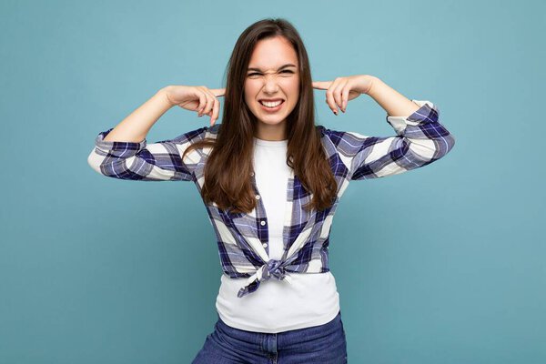 Dont want to hear it. Young emotional positive attractive brunette female person isolated on blue background with copy space and covering ears