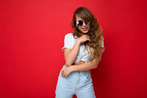 Foto-Foto von schönen sexy positive junge blonde Frau trägt lässige Kleidung und stilvolle Sonnenbrille isoliert über bunten Hintergrund Blick auf die Kamera — Stockfoto