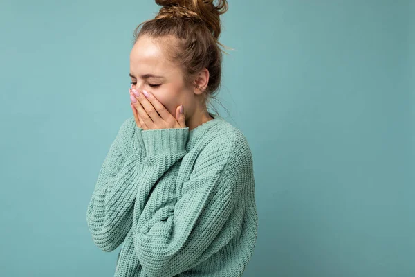 Retrato de una joven riéndose positiva guapa rubia guapa con emociones sinceras vistiendo un suéter azul de moda aislado sobre fondo azul con espacio libre y boca cubierta — Foto de Stock