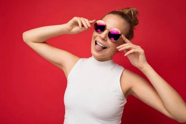 Foto de hermosa mujer rubia feliz usando ropa casual y gafas de sol con estilo aislado sobre fondo colorido mirando a la cámara y divertirse — Foto de Stock