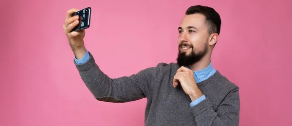 Panoraama kuva Komea nuori mies yllään rento tyylikkäät vaatteet seisoo eristetty taustan yli seinän tilalla älypuhelin selfie valokuva katselee matkapuhelimen näytön — kuvapankkivalokuva
