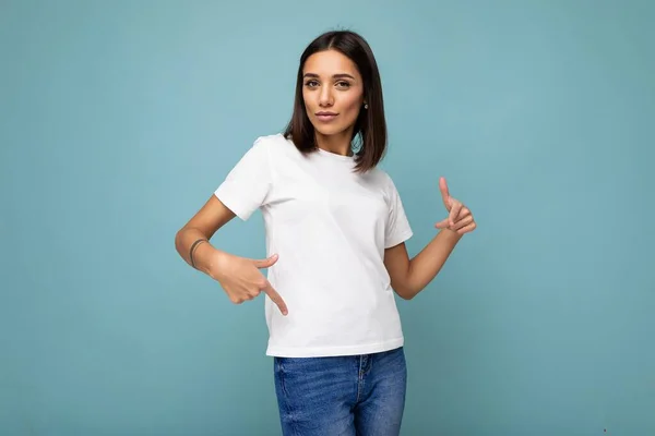 魅力的な自信を持って若いですブルネット女性でカジュアルホワイトtシャツのためにモックアップ隔離された青の背景にフリースペース — ストック写真