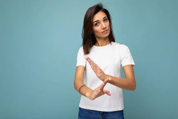 Retrato de jovem bela mulher morena com emoções sinceras vestindo camiseta branca na moda para maquete isolado em fundo azul com espaço vazio e fazendo gesto de tempo limite. Conceito de pausa — Fotografia de Stock