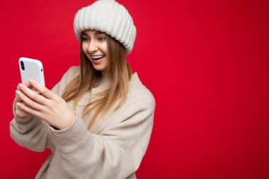 Çekici, mutlu, gülümseyen, sıradan, şık kıyafetler giyen, arka planda izole edilmiş, el ele tutuşmuş ve cep telefonu mesajları kullanan genç bir kadının fotoğrafı.